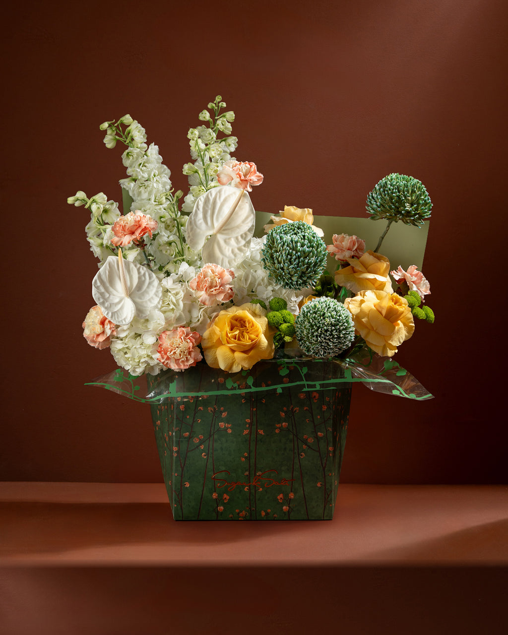 Floral arrangement in a green box against a brown background