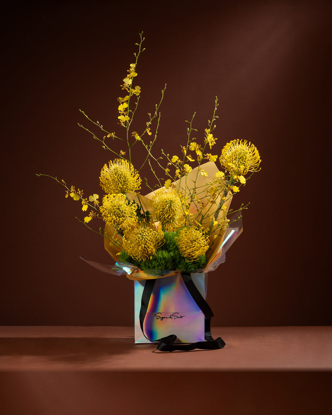 Bouquet of yellow flowers in a transparent box with a colorful label on a dark background
