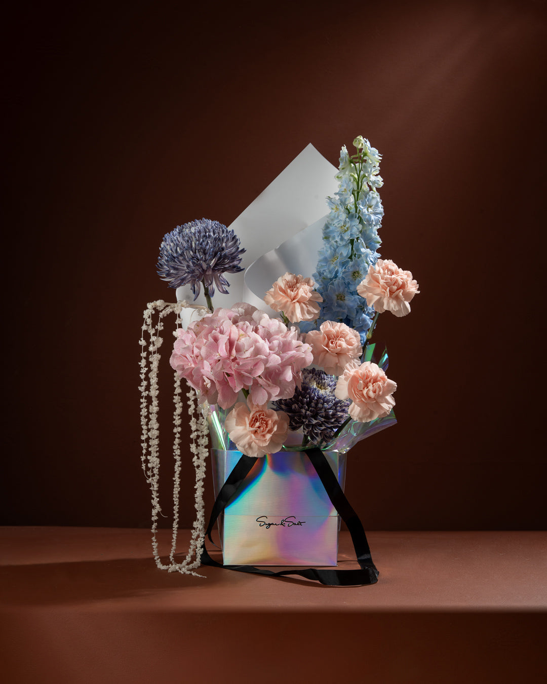 Bouquet of flowers in a colorful box with a necklace on a brown background