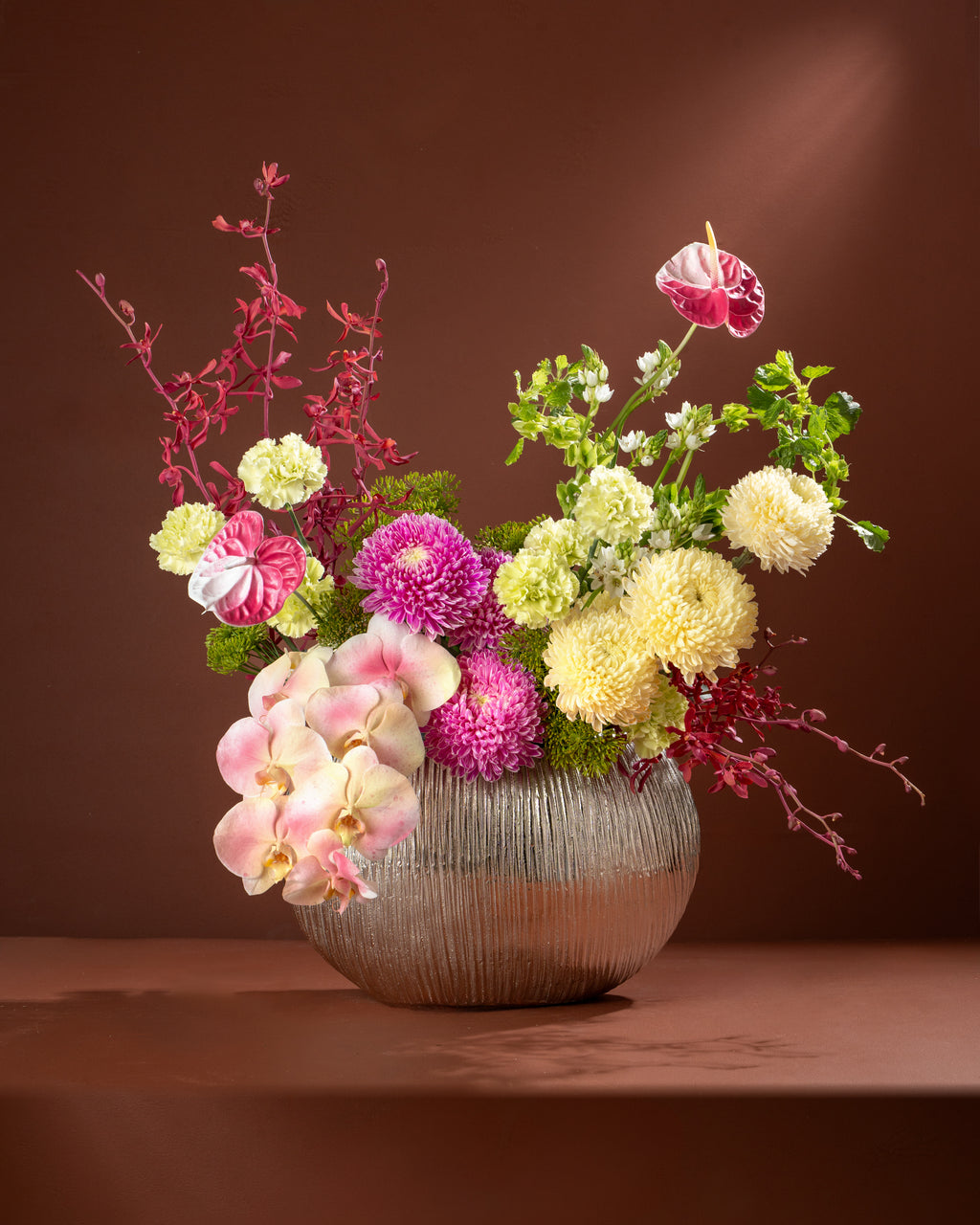Floral arrangement in a silver vase on a brown background
