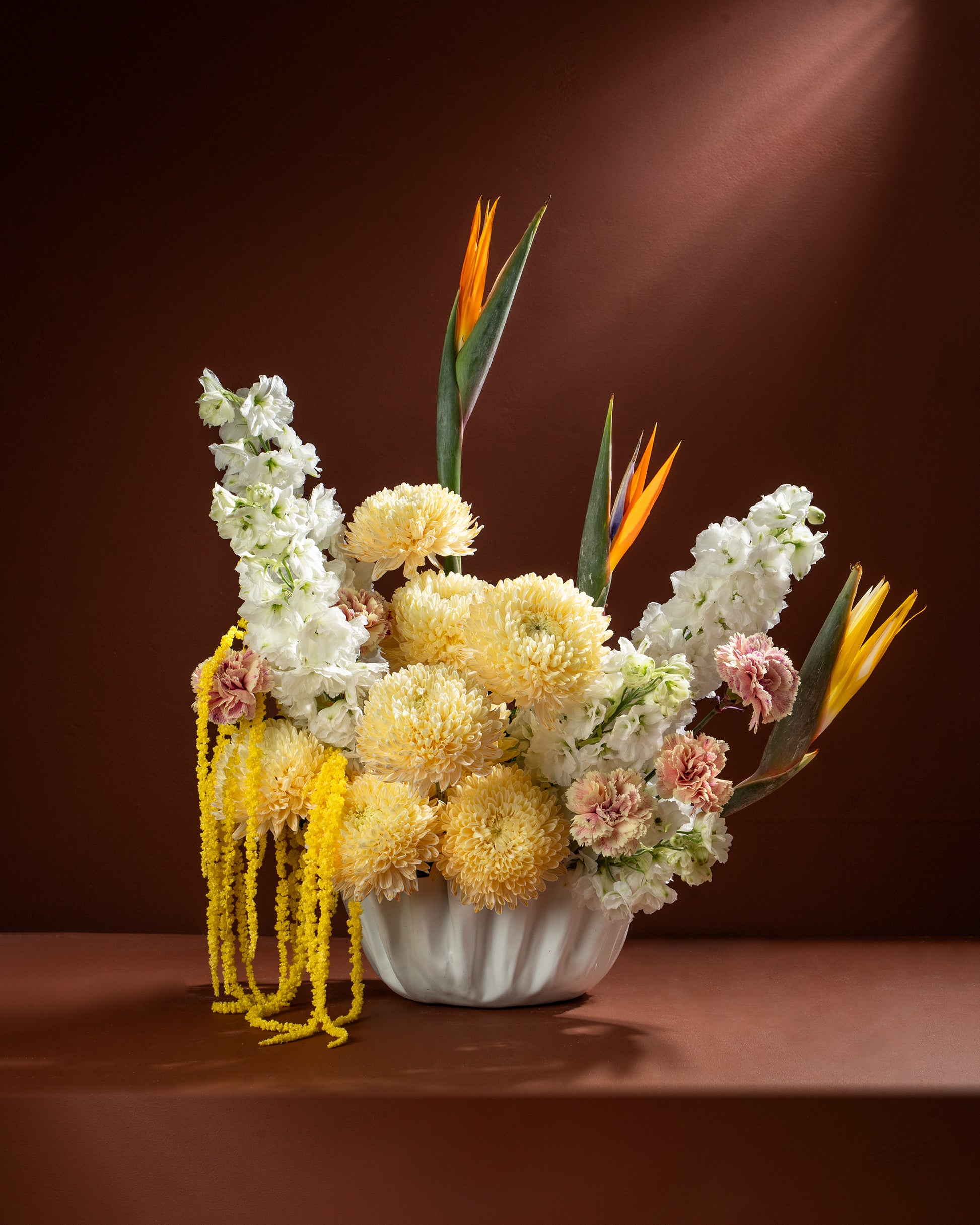 Floral arrangement with yellow, white, and pink flowers in a white vase on a brown background