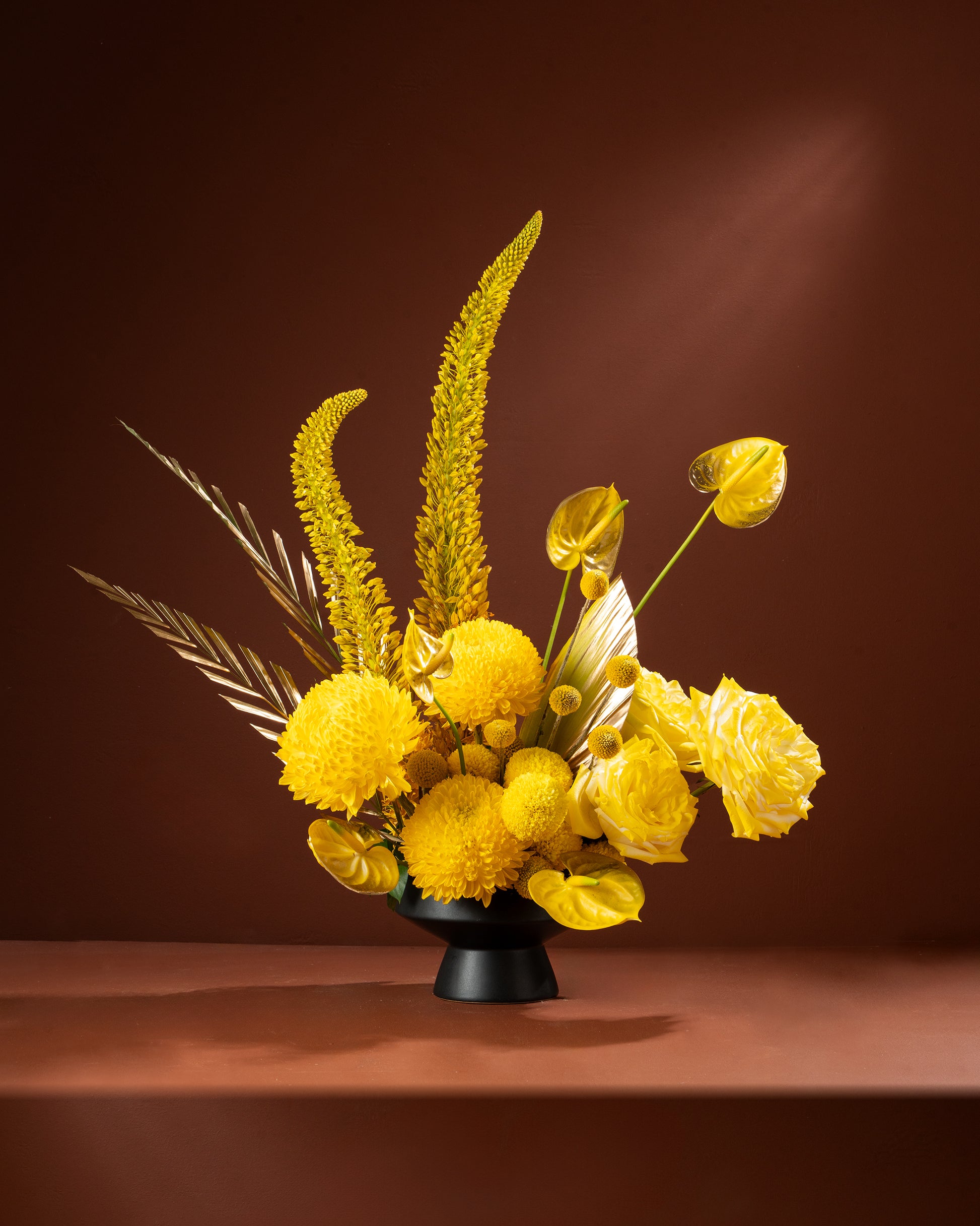 Yellow floral arrangement in a black vase on a brown background