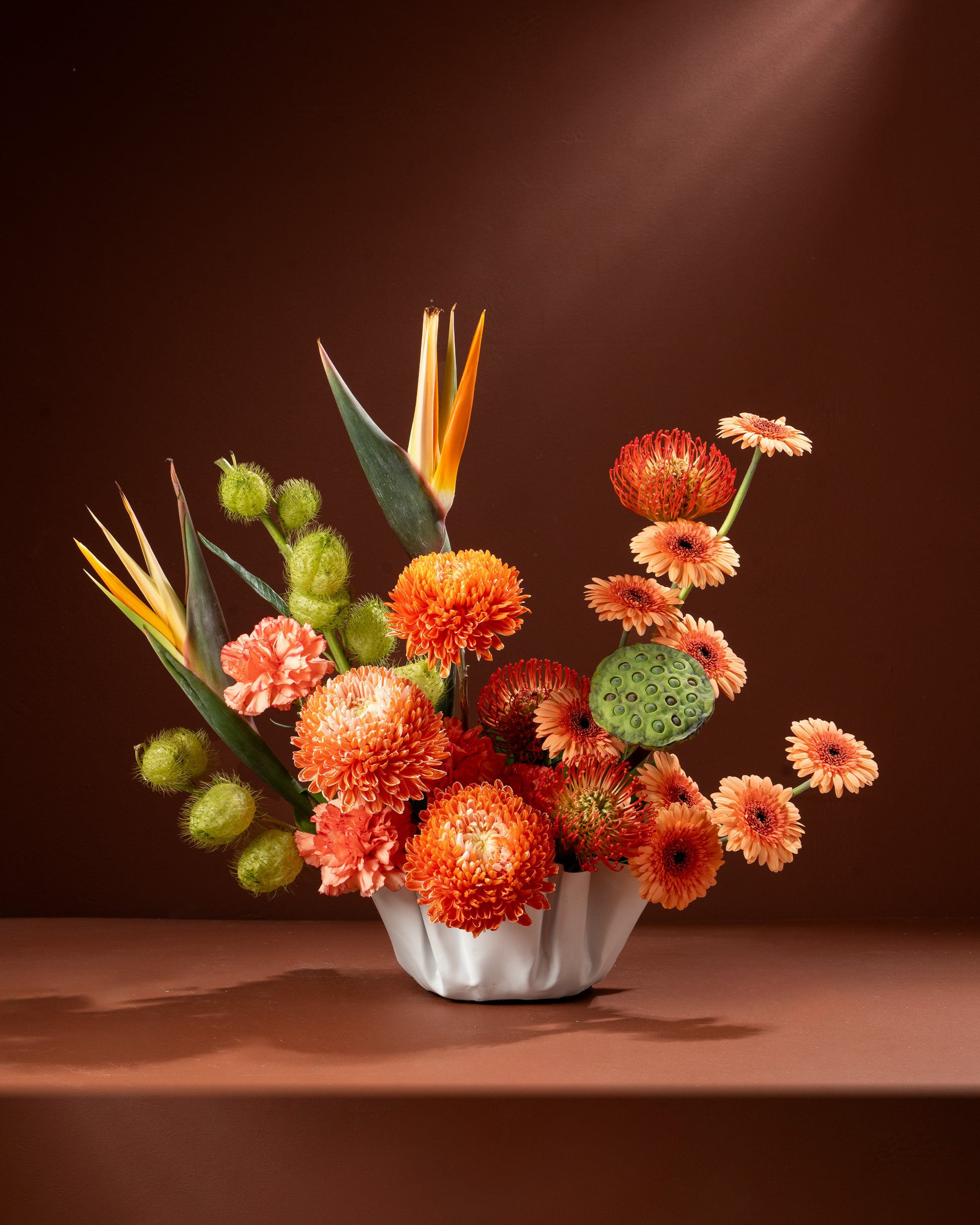 Floral arrangement with orange and green flowers in a white vase on a brown background