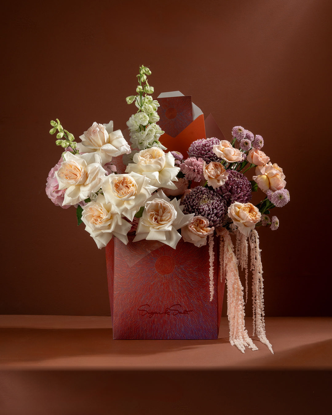 Floral arrangement in a decorative box with a brown background