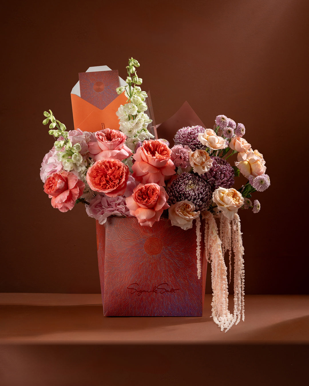 Floral arrangement in a decorative box on a brown background