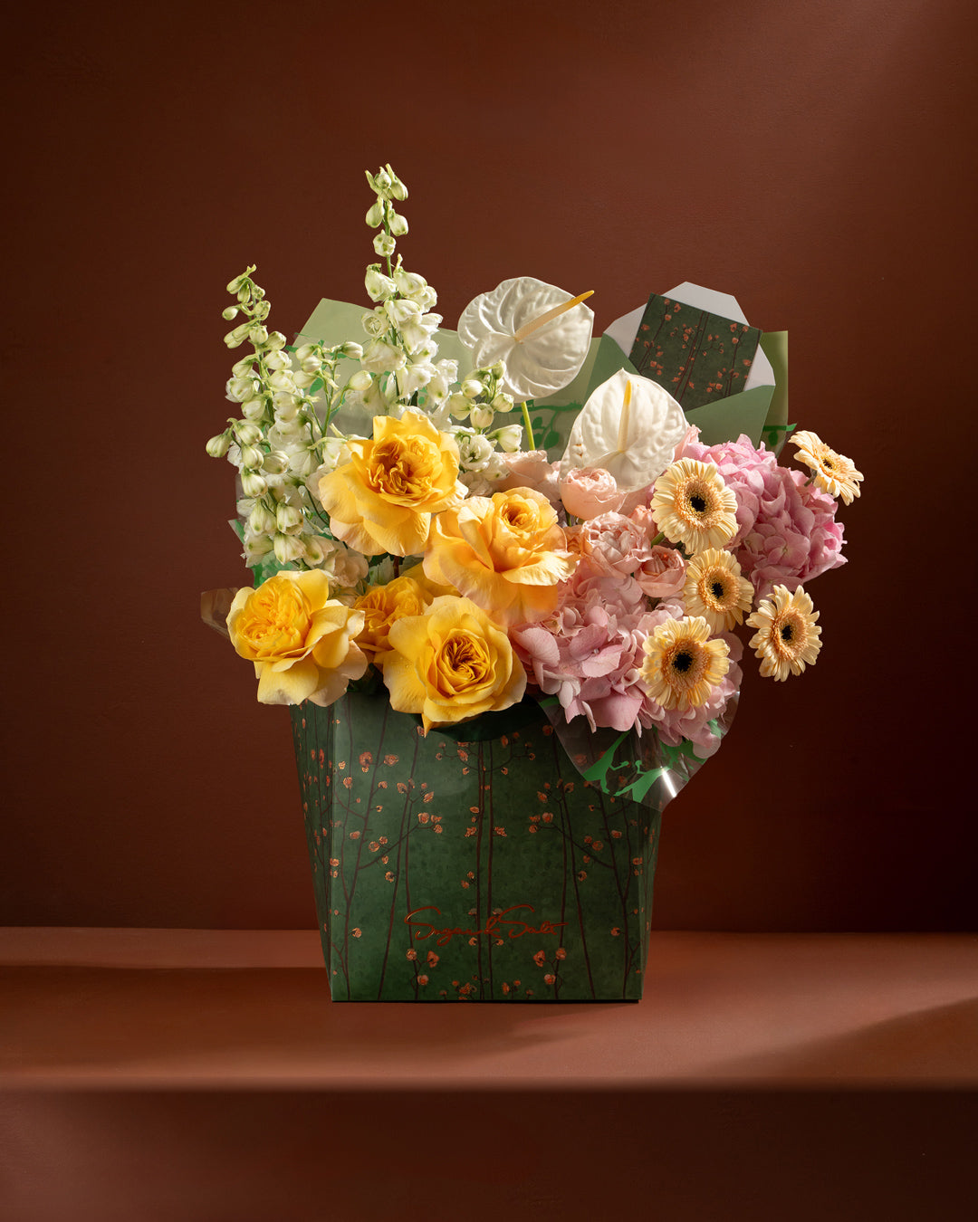 Bouquet of flowers in a green box against a brown background