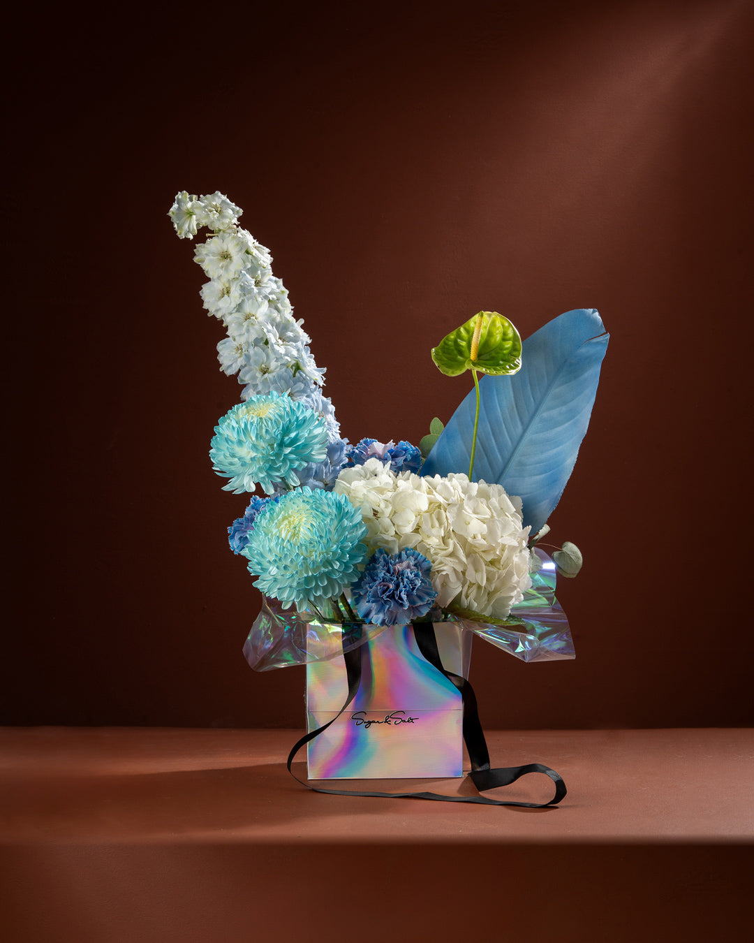 Floral arrangement with blue and white flowers in a colorful box on a brown background